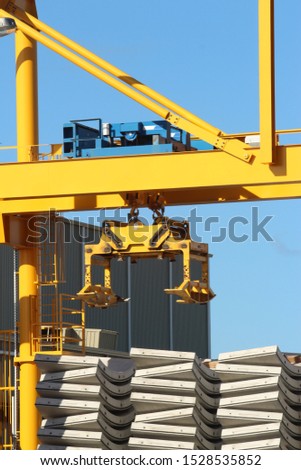 Outdoor yellow overhead crane with pre cast concrete segments stacked below. Tunnel making factory and warehouse. Blue sky background