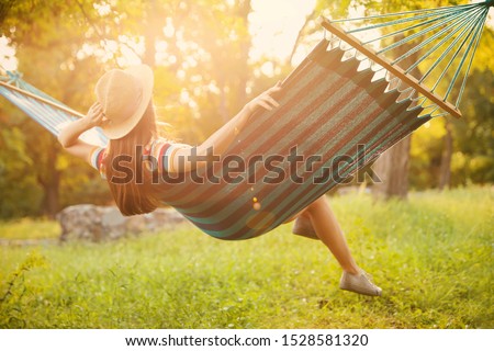 Young woman resting in comfortable hammock at green garden Royalty-Free Stock Photo #1528581320