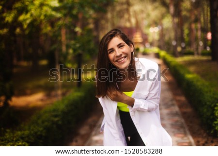Portrait beauty woman walking on the park. Girl looks free in white shirt, neon green top and shorts. Woman with short hair. Woman look happy and smiling. Concept of freedom and unity with nature.