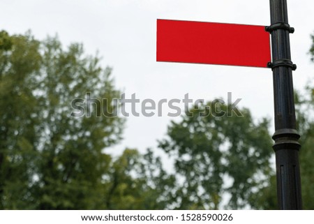 empty red signboard on an iron pole against a light sky and treetops with copy space for your text. blank information sign mock-up