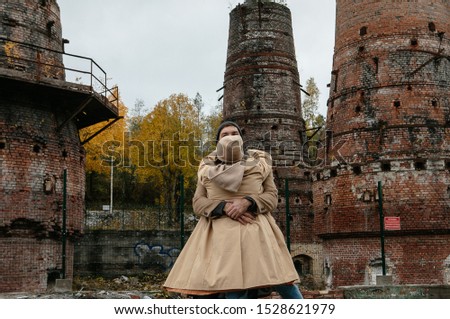 unusual couple in love in a brown coat running and cuddling in an abandoned city against a background of destroyed brick ovens of a factory, autumn travel to the north of Russia, apocalypse