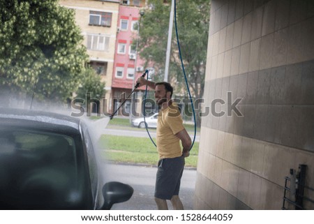 Rinsing the car after some heavy washing.  Man washing car.
