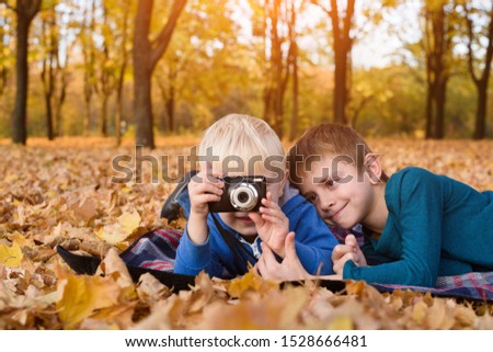 Two little brothers take a pictures on the camera. Lying in yellow autumn leaves. Fall day