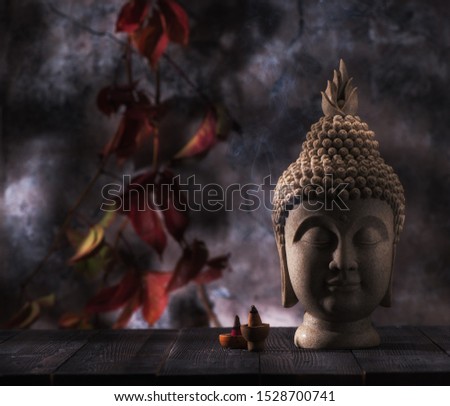 Buddha head statue and incense on a background red leaves. Buddhism and meditation concept