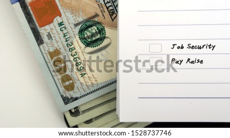 Cash dollars money and lined paper notebook with checkbox choices to choose between  JOB SECURITIES and PAY RAISE - concept of making decision in career move