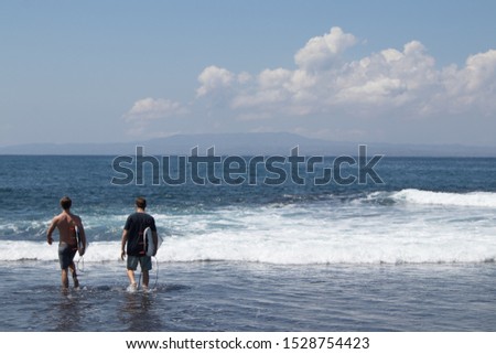 Two surfers walking with their board under their arm towards a sea full of waves.