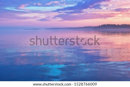Misty seascape - calm water surface of the lake reflects lilac sky with pink and blue clouds after sunset. White nights season in the Republic of Karelia, Russia. Blur filter, space for copy. Royalty-Free Stock Photo #1528766009