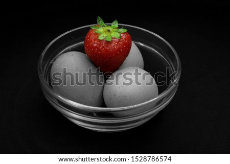 Black and white photograph of three eggs with colourful strawberry on top in a bowl.