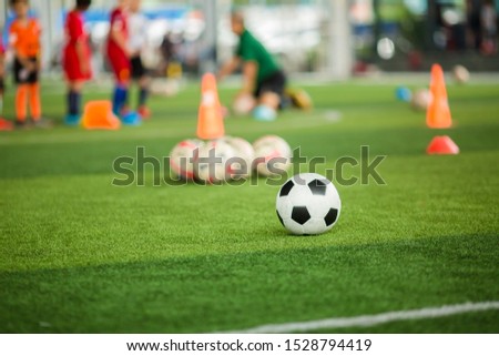 Soccer ball on green artificial turf with blurry soccer team training. Blurry kid player training and soccer equipment in soccer academy.