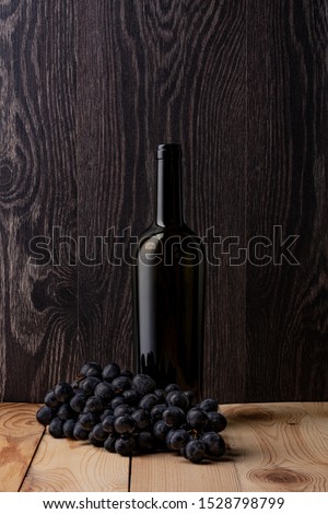 Wine bottle and a glass of wine. A bunch of ripe black grapes. Wooden background.