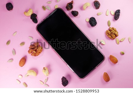 A picture of  blank smartphone with variety  of nuts and pink background.