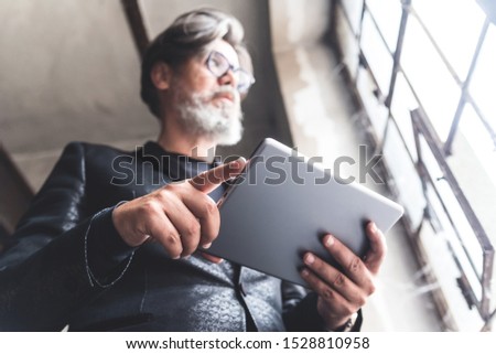 Concentrated businessman with a view out the window in suit using tablet in old hall because of job. Closeup picture. Blurred image.