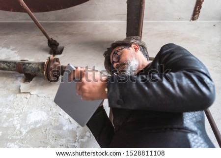 Concentrated businessman in suit using tablet in old hall because of job. He is pictured from below