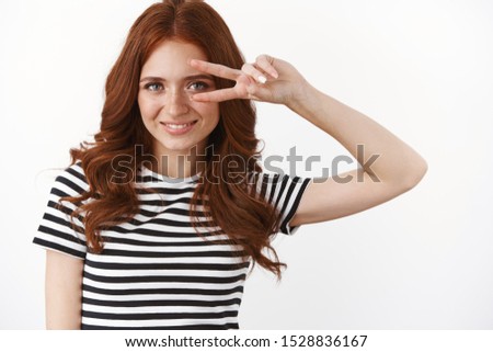 Close-up shot motivated and ambitious good-looking redhead woman in striped t-shirt, express confidence show victory, peace or goodwill sign over eye, smiling pleased, standing self-assured