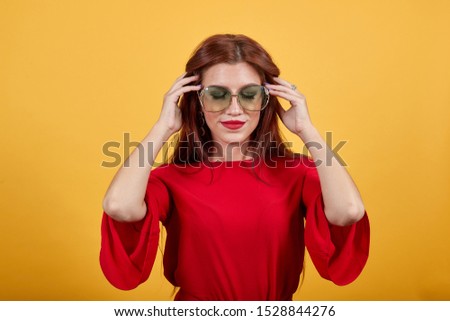 Beautiful girl with closed eyes wearing brown sunglasses. Cute lady in red garment holding glasses protecting from sun with her fingers of both hands.