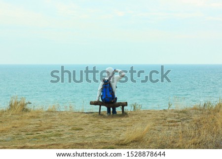 A young man travels alone. Solo travelling. A tourist sits on a wooden bench on a cliff above the sea coast and looks at the horizon. Loneliness, lifestyle vacations concept.