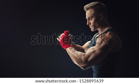 Man is wrapping hands with red boxing wraps isolated on black background Strong hands and fist, ready for training and active exercise