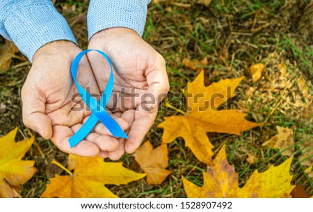 Men's health and prostate cancer awareness in November. A man holding a light blue ribbon on a background of autumn leaves. A symbol of support for men who live with cancer.  Copy space.