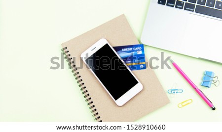 Above of office items on desk with laptop, pen, smartphone, credit card and notebook with copy space green background. flat lay style. top view photo.