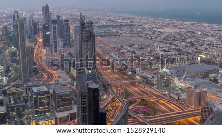 Dubai Downtown skyline futuristic cityscape with many skyscrapers and traffic on intersection aerial night to day transition timelapse. Morning panorama with modern towers and construction from