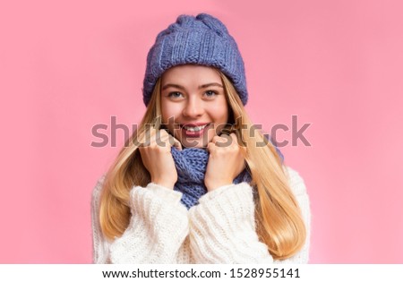 Portrait of beautiful smiling girl in blue knitted winter set over pink background