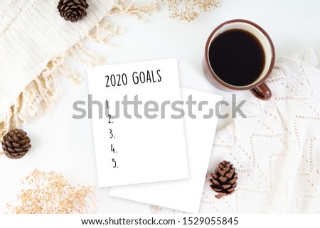 Hot cup of coffee and pine tree serve on white bed sheet in the morning top view with paper note writing of text 2020 goals list for new year resolutions.