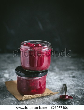 Glass of berry cherry sauce with vintage spoon on the paper on the gray cement background. Copy space.
