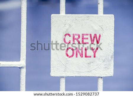 Crew only sign on a ferry boat. Red stenciled letters against a white metal square attached to railings,against a blue background.