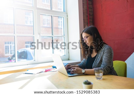 Female in casual wear and glasses experienced business writer for executive summary typing article on pc laptop computer while sitting in modern office near window with copy space for advertising  