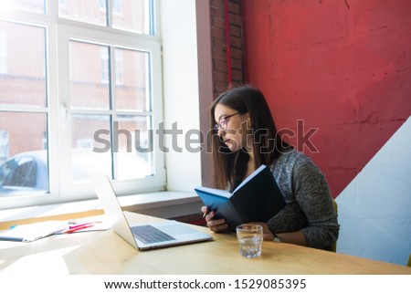 Female in spectacles smart university student having online learning via pc laptop computer, sitting in library. Hipster girl having training course via notebook gadget, sitting in co-working 