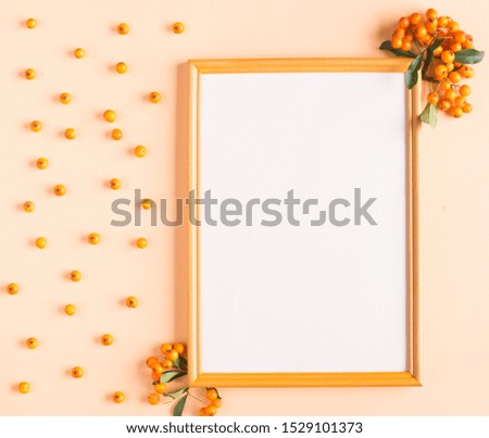 Autumn composition of a wooden frame and orange rowan berries on a yellow paper background top view copy space