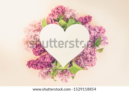 Fresh lilac flowers over pink background with copy space on heart shaped paper note, flat lay floral composition, toned