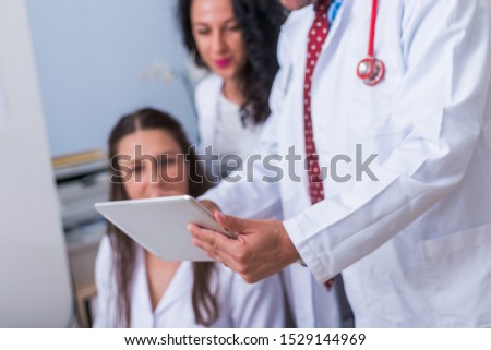Two nurses, female physicians and a male doctor looking in a tablet at the doctor's office while discussing a medical report ( patient's health problems. defocused, blurred view