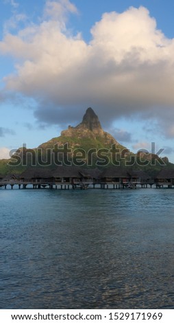 Panorama view on luxury overwater bungalows in a vacation resort in the blue lagoon with in the background the tropical island of Bora Bora, near Tahiti, in the pacific archipelago French Polynesia.
