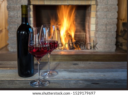 Two glasses of wine and wine bottle near cozy fireplace, in country house, winter vacation.