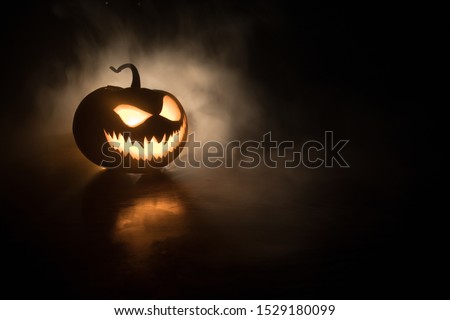 Halloween pumpkin smile and scary eyes for party night. Close up view of scary Halloween pumpkin with eyes glowing inside at black background. Selective focus Royalty-Free Stock Photo #1529180099