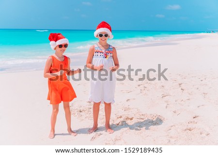 Little adorable girls in Santa hats having fun anad fooling at Christmas on the beach