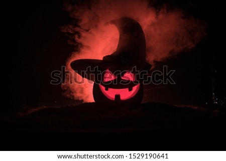 Halloween concept. Jack-o-lantern smile and scary eyes for party night. Close up view of scary pumpkin with witch hat on at dark foggy background. Selective focus. Empty space
