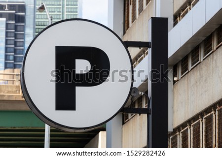 Parking (P) sign on a pole in-front of a parking garage in a big city. 