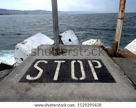 The word Stop painted on the pavement floor of a concrete pier 