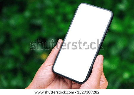 Mockup image of hands holding black mobile phone with blank desktop screen with green nature background