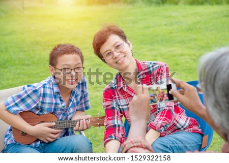 Asian Senior male taking photo his wife and son by smart phone while they’re on vacation camping.