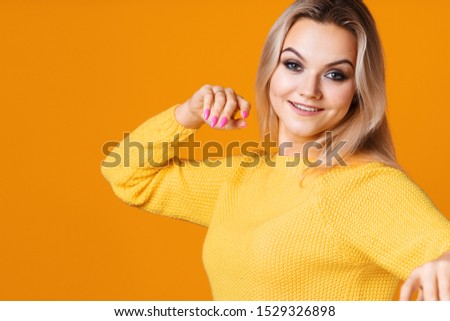 Happy and cheerful blonde in a yellow sweater on a yellow background. Positive young woman rejoices and dances, portrait close-up. copy space