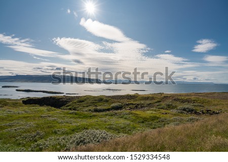 Blue and green misty mountains surrounding still bay, overlooking small farmland, Westjords Iceland