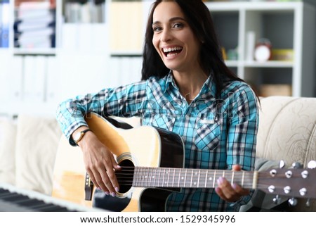 Portrait of wonderful female studying new melody and playing in studio. Beautiful lady wearing checkered fashionable blouse. Music and art concept. Blurred background