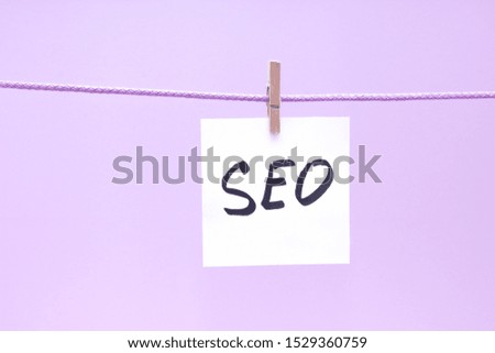 The note is written on a white sticker that hangs with a clothespin on a rope on a yellow colored background
