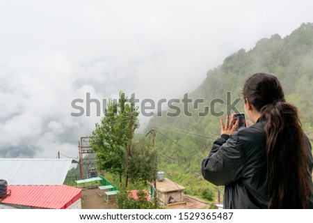Young indian girl shooting photos of clouds at a hill station using her phone. Influencers today shoot their trips for images, vlogs, videos and post it for their follower base