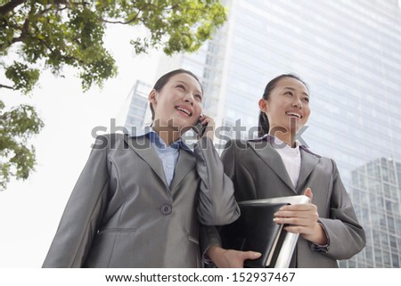 Two young businesswomen walking down the street and talking on the phone
