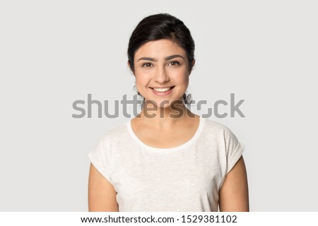 Headshot portrait of happy indian millennial girl stand isolated on grey studio background wear t-shirt look at camera, smiling ethnic young woman posing showing white healthy teeth, dental treatment Royalty-Free Stock Photo #1529381102