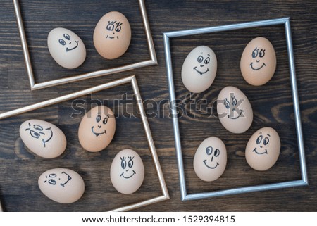 Picture golden frame and many funny eggs smiling on dark wooden wall background, close up. Eggs family emotion face portrait. Concept funny food